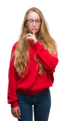 Blonde teenager woman wearing red sweater asking to be quiet with finger on lips. Silence and secret concept.