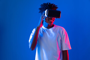 Surprised young African American looking through VR holding interesting object hologram on pink...