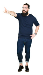 Young hipster man with long hair and beard wearing glasses Pointing with finger surprised ahead, open mouth amazed expression, something in front