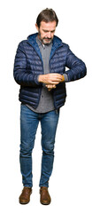 Fototapeta premium Middle age handsome man wearing winter coat Checking the time on wrist watch, relaxed and confident