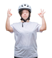 Young adult cyclist woman with down syndrome wearing safety helmet over isolated background relax and smiling with eyes closed doing meditation gesture with fingers. Yoga concept.