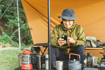 キャンプ場でスマホを使う中年男性キャンパー（キャンプ場・アプリ）

