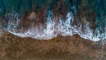 Drone view above ocean waves near the islands of Taha'a and Bora Bora in French Polynesia. The clear blue sea water is disrupted by white cap current. 