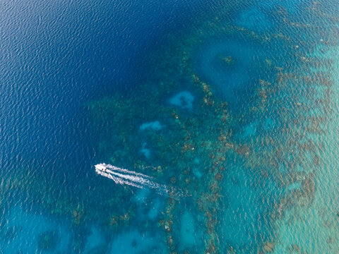 Aerial drone view of a small boat racing through vibrant blue ocean water above a coral reef in Bora Bora, French Polynesia. 