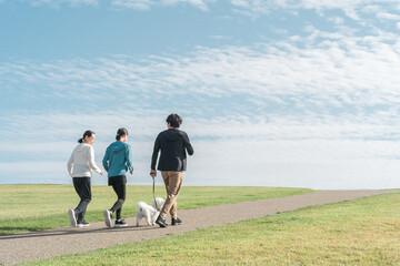 Obraz premium 青空の見える公園で犬の散歩・運動・トレーニング・有酸素運動をするさわやかな家族・親子 