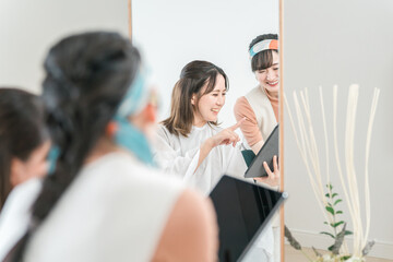 美容室・ヘアサロンでタブレットを使いヘアスタイル・髪型を相談する客の女性とカウンセリングする美容師
