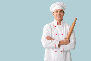 Handsome happy male chef with rolling pin on blue background