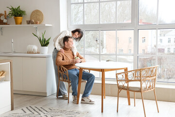 Young woman hugging her husband with cup of coffee in kitchen