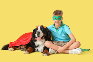 Cute fluffy dog and boy in superhero costumes on yellow background