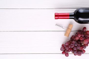 Corkscrew, bottle of wine and grapes on white wooden table, flat lay. Space for text