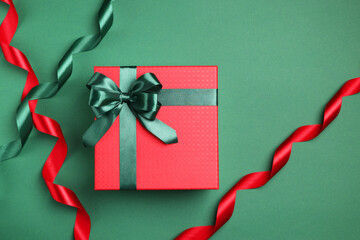 Beautiful red gift box with bright bow and ribbons on green background, flat lay