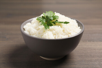 Bowl of delicious boiled rice with parsley on wooden table