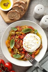 Delicious fresh burrata salad in bowl served on gray textured table, flat lay