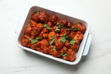 Baked cauliflower buffalo wings with parsley in baking dish on white marble table, top view