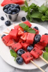 Skewers with tasty watermelon, strawberries, blueberries and mint on light table, closeup