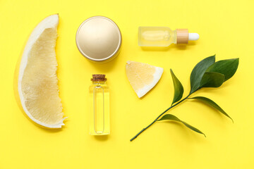 Bottles, jar of cosmetic product, green leaves and pieces of fresh pomelo on yellow background