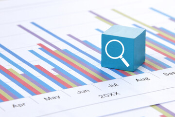 チャートの上に置かれた虫眼鏡のアイコンが描かれたブロック