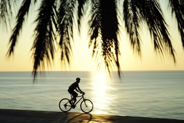 Fototapeta premium Sunset silhouette cyclist on beach, palm tree shadows, healthy evening cycling by ocean coast