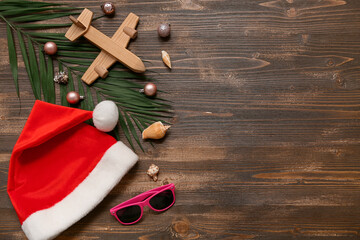 Santa's hat, wooden airplane, sunglasses and palm branch with Christmas balls and shells on wooden background. Top view