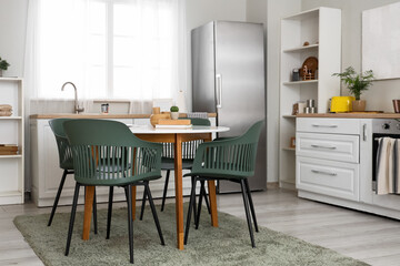 Interior of light kitchen with fridge, white counters with oven and dining table