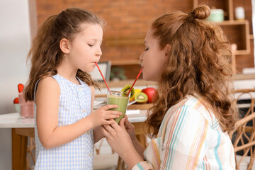 Mother and little daughter drinking smoothie from one glass in kitchen