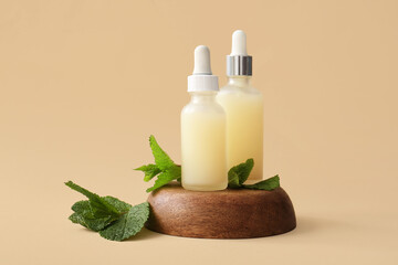 Bottles of essential oil, wooden stand and mint leaves on beige background