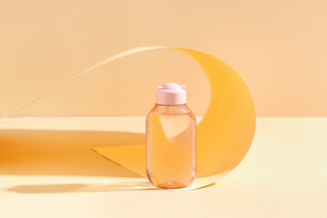 Bottle of micellar water and folded paper sheet on pale yellow background