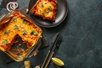 Composition with tasty enchilada, spices and cutlery on dark color background