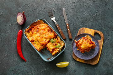 Composition with tasty enchilada, spices and cutlery on dark color background