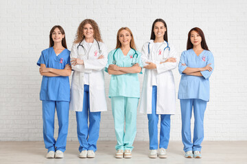 Female doctors with pink ribbons on white brick background. Breast cancer awareness concept