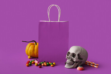 Paper shopping bag, decorations and candies for Halloween on purple background