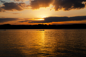 Fototapeta premium Orange sunset reflected in Lake Chickamauga with a jet ski speeding through the sun's reflection