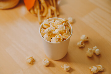 A bucket of popcorn, top-view, warm colors, light brown wooden background, flat lay, daylight macro close-up