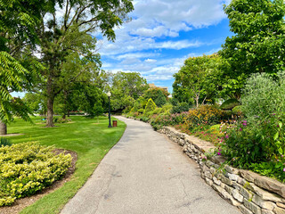 Park nature path stone walls natural landscaping bushes flowers trees blue sky clouds green grass