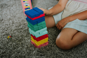 girl plays Jenga using colored pieces of wood on a gray carpet at home 