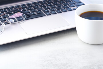 コーヒーを飲みながらノートパソコンでデスクワークをしているイメージ
