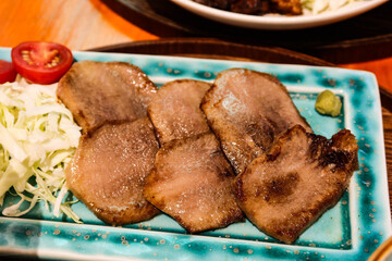 close up of Japanese sliced grilled ox beef tongue on a blush green plate with cabbage and cherry tomato on the side