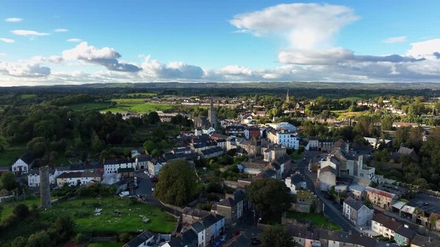 Clones Town, County Monaghan, Ireland, April 2023. Drone pulls backwards across old buildings revealing the Round Tower cemetery nestled between homes and businesses.
