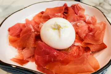 close up of cold cut Burrata cheese with parma ham on a white plate