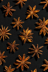 Brown Anise stars as pattern at sunlight, top view close up aromatic spices dried aniseed on black background, minimal aesthetic food, textural graphic photo, natural season condiments
