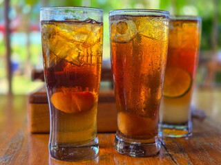 Iced lemon tea and lychee on wooden table, blurred natural background