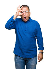 Middle age arab man wearing glasses over isolated background doing ok gesture shocked with surprised face, eye looking through fingers. Unbelieving expression.