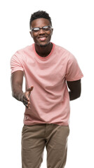 Fototapeta premium Young african american man wearing pink t-shirt smiling friendly offering handshake as greeting and welcoming. Successful business.