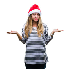 Young beautiful blonde woman wearing christmas hat over isolated background clueless and confused expression with arms and hands raised. Doubt concept.