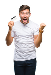 Young handsome man holding credit card over isolated background screaming proud and celebrating...