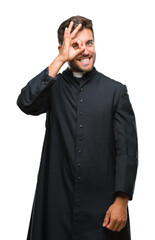 Young catholic christian priest man over isolated background doing ok gesture with hand smiling, eye looking through fingers with happy face.