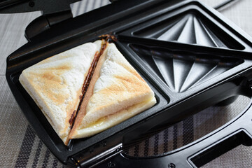 Close up of hot sandwich ham and cheese on a toaster for making hot sandwich toast breakfast. Bread and toaster on the kitchen table.