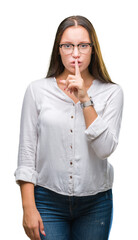 Young caucasian beautiful business woman wearing glasses over isolated background asking to be quiet with finger on lips. Silence and secret concept.