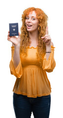 Fototapeta premium Young redhead woman holding passport of Germany surprised with an idea or question pointing finger with happy face, number one