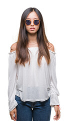 Young asian woman wearing sunglasses over isolated background with serious expression on face. Simple and natural looking at the camera.
